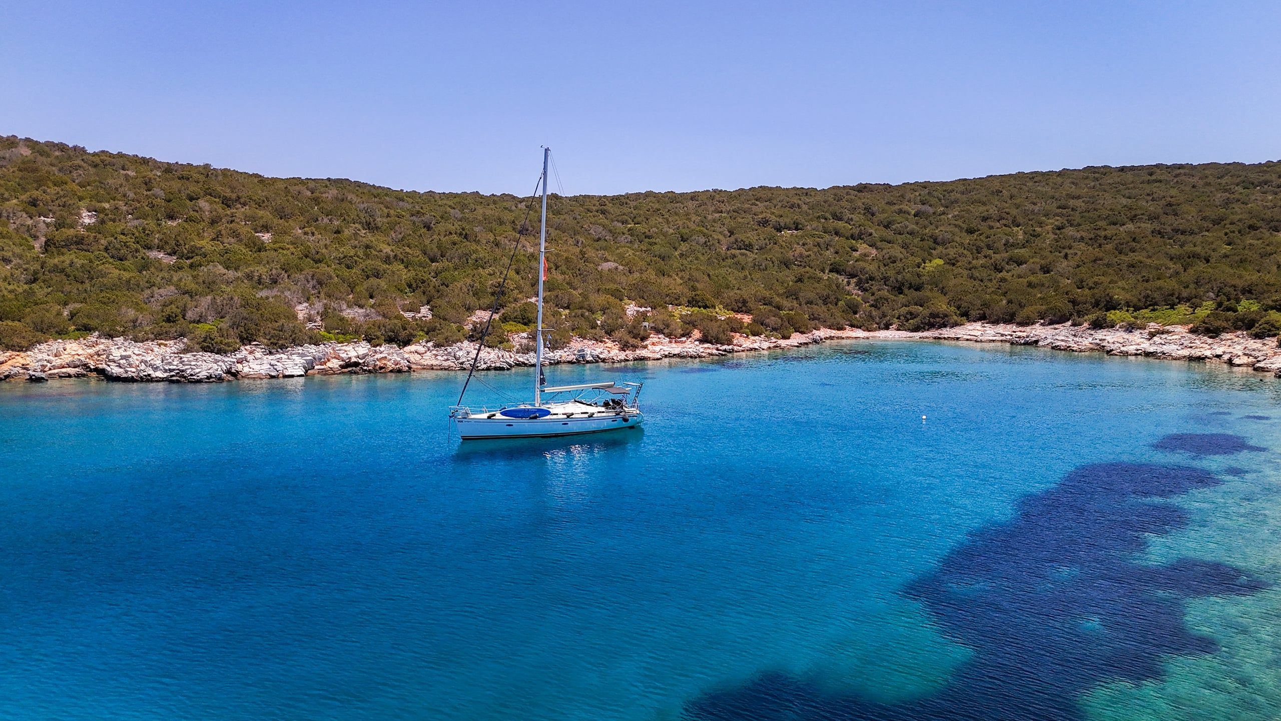 Sailing yacht anchored alone in a quiet bay below scrub-covered hills
