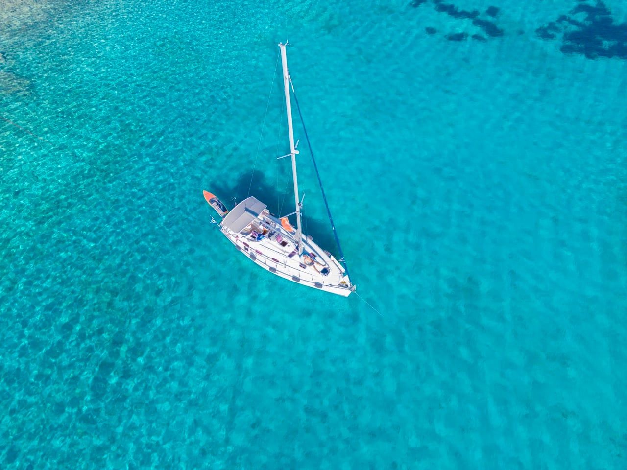 Sailing yacht anchored alone in bright turquoise water, seen from above