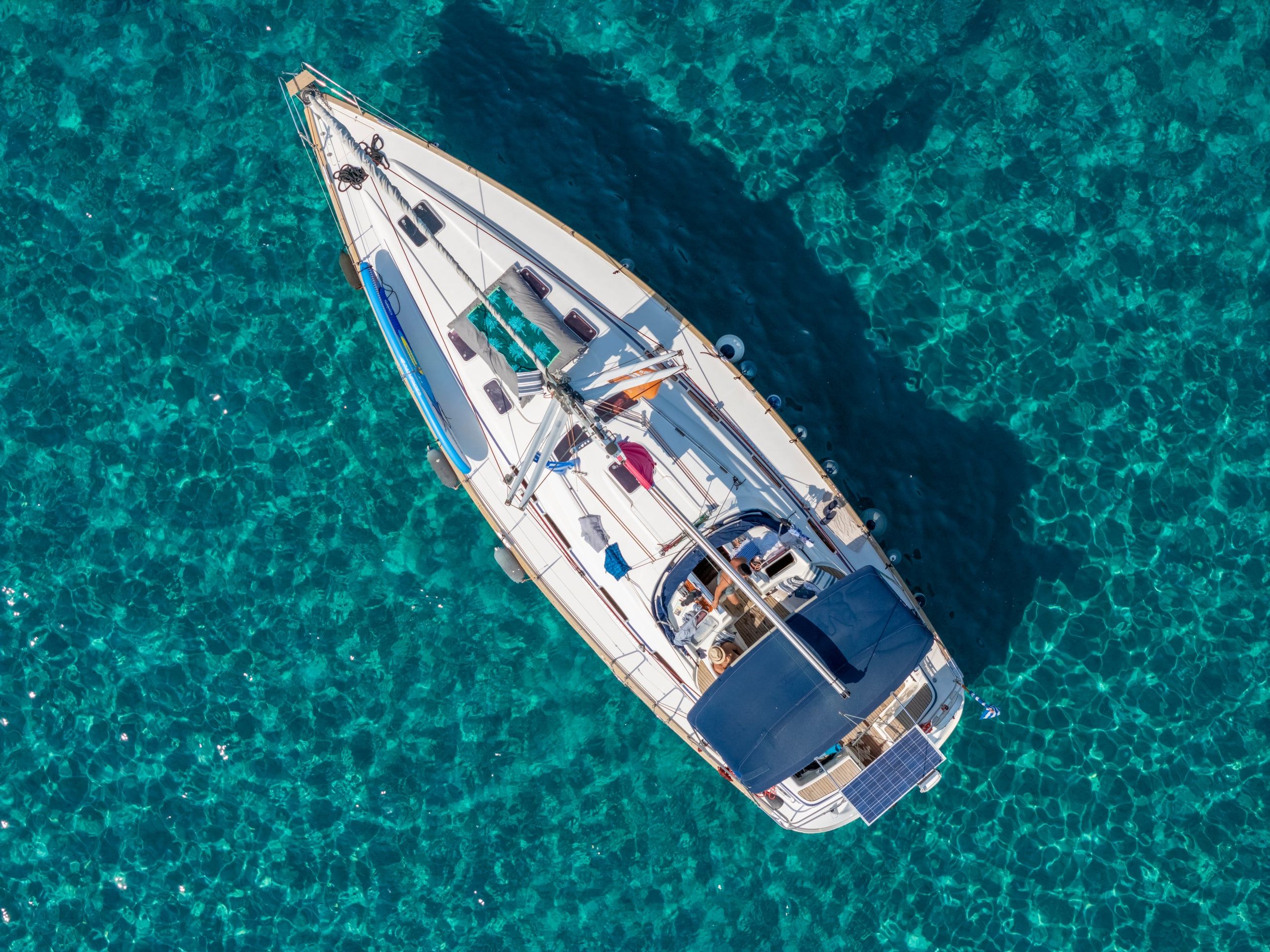 Sailing yacht at anchor over rippled turquoise water, seen from directly above