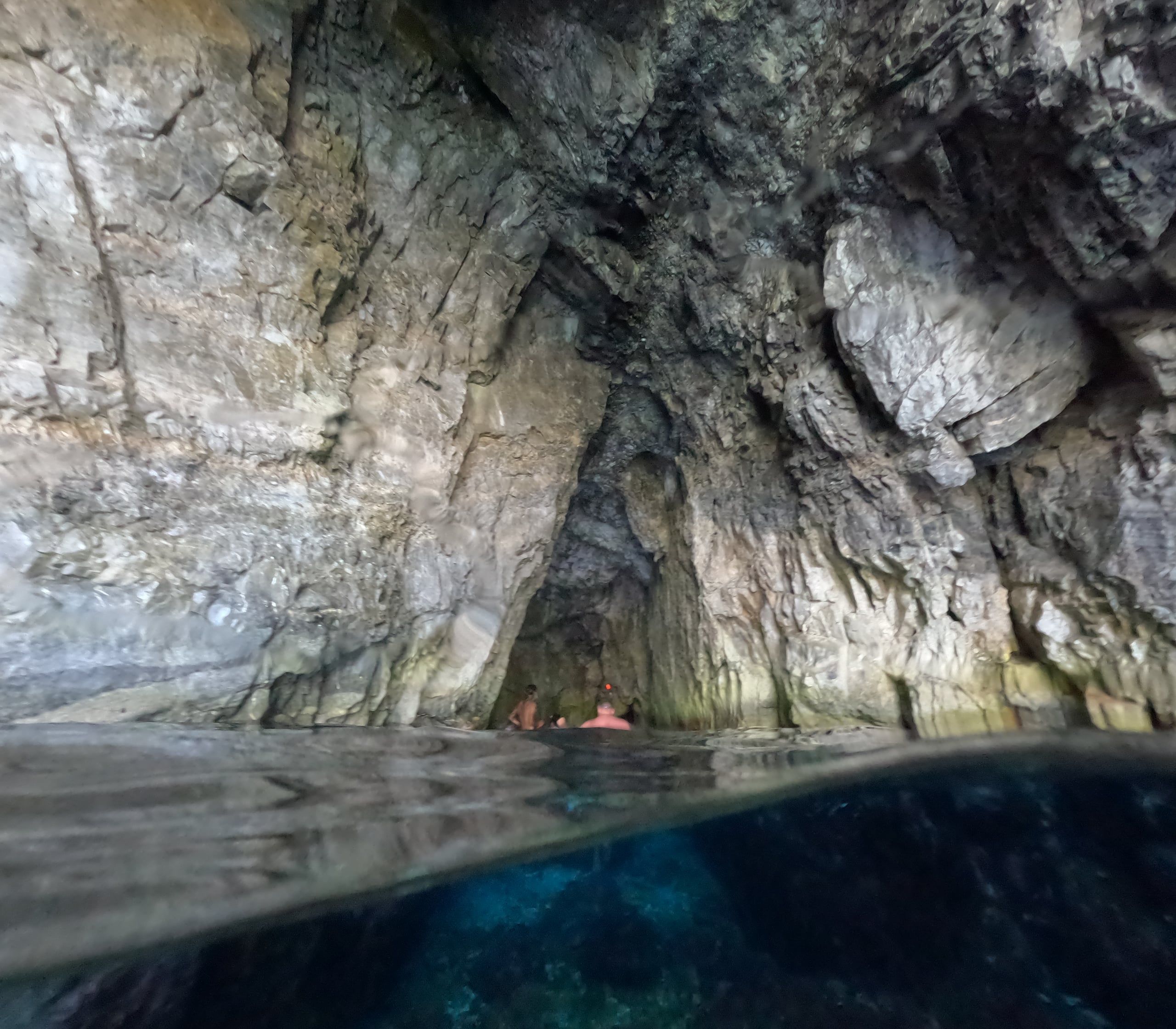 Swimmers inside a sea cave over clear water, seen from the surface