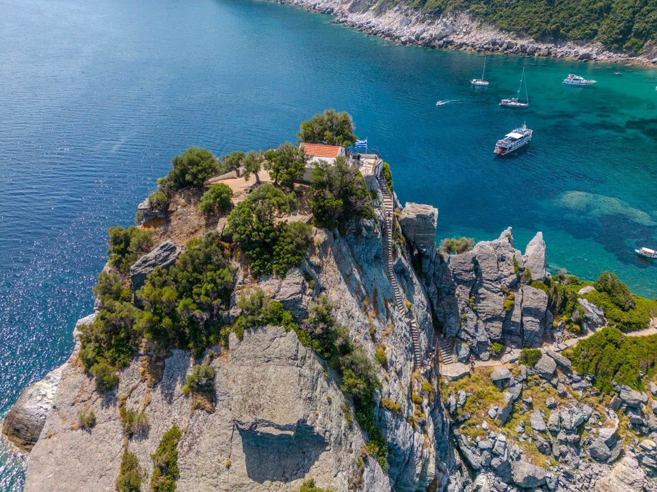 Chapel of Agios Ioannis on its rock above a blue bay with boats on Skopelos