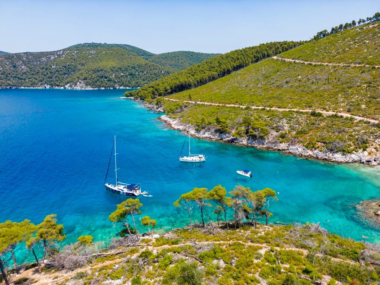 Two sailing yachts anchored in a blue bay below green hills near Agnontas on Skopelos