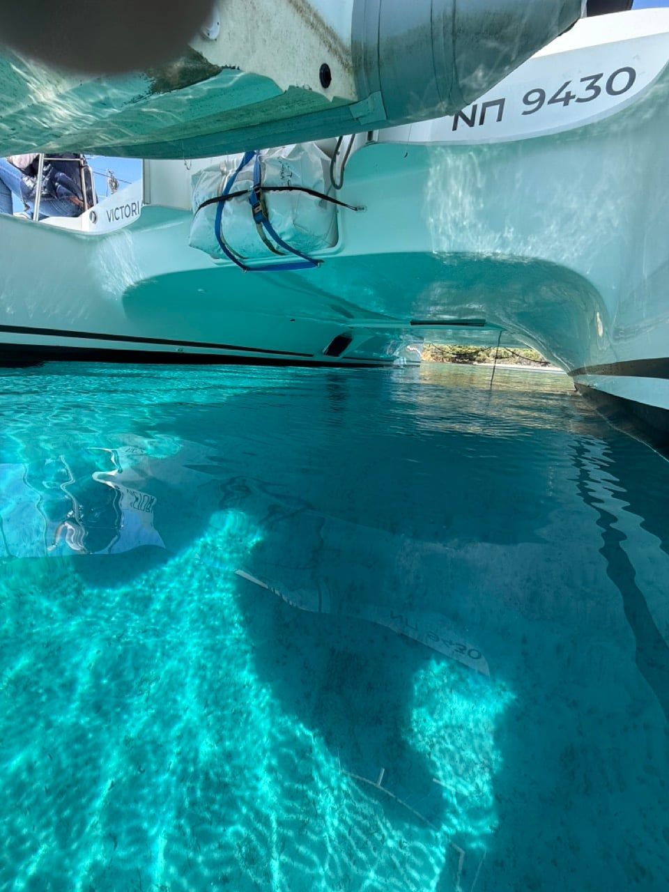 View between the hulls of a catamaran and under its deck over clear turquoise water