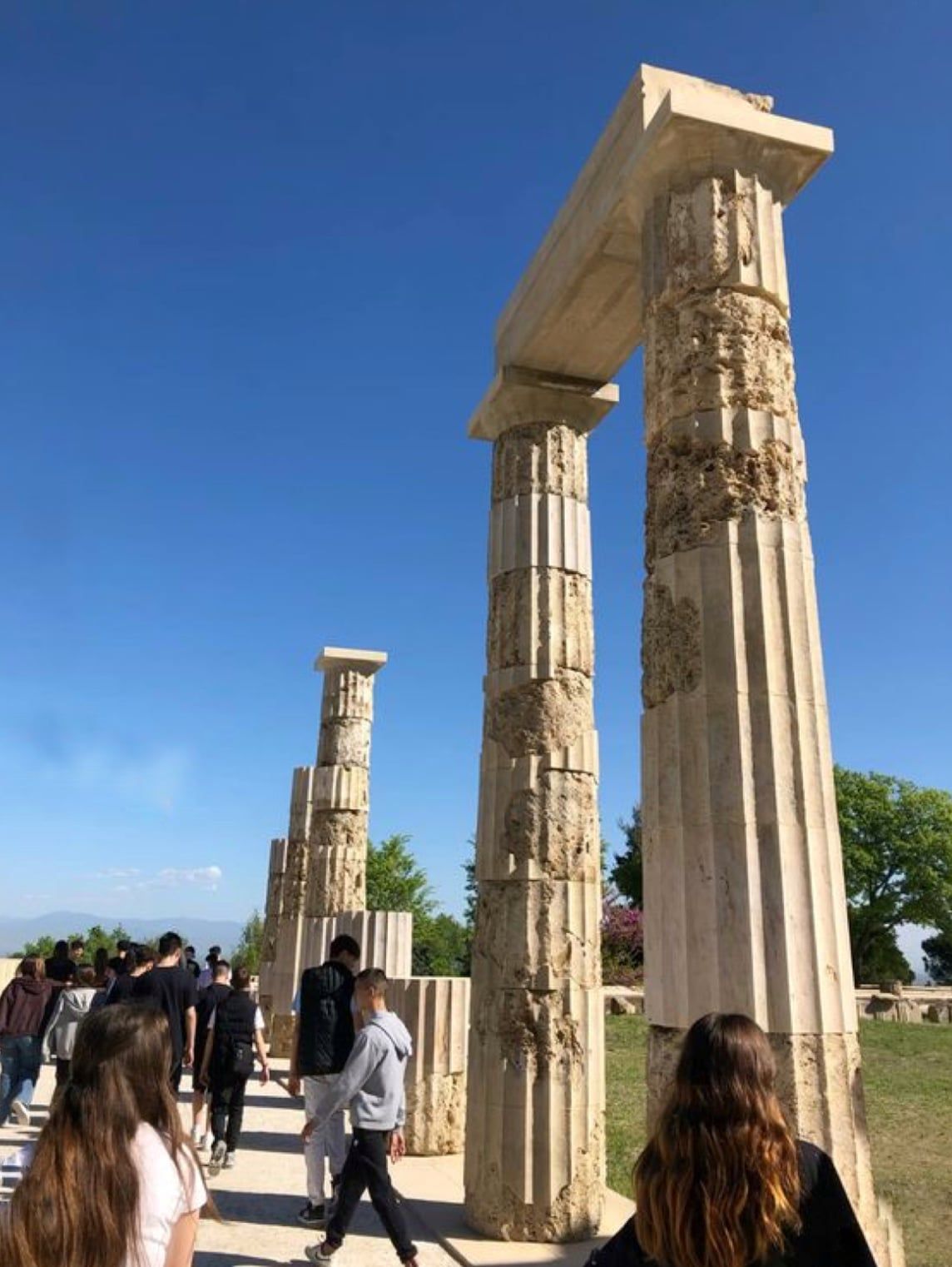 Visitors walking past tall restored stone columns at the ancient site of Vergina
