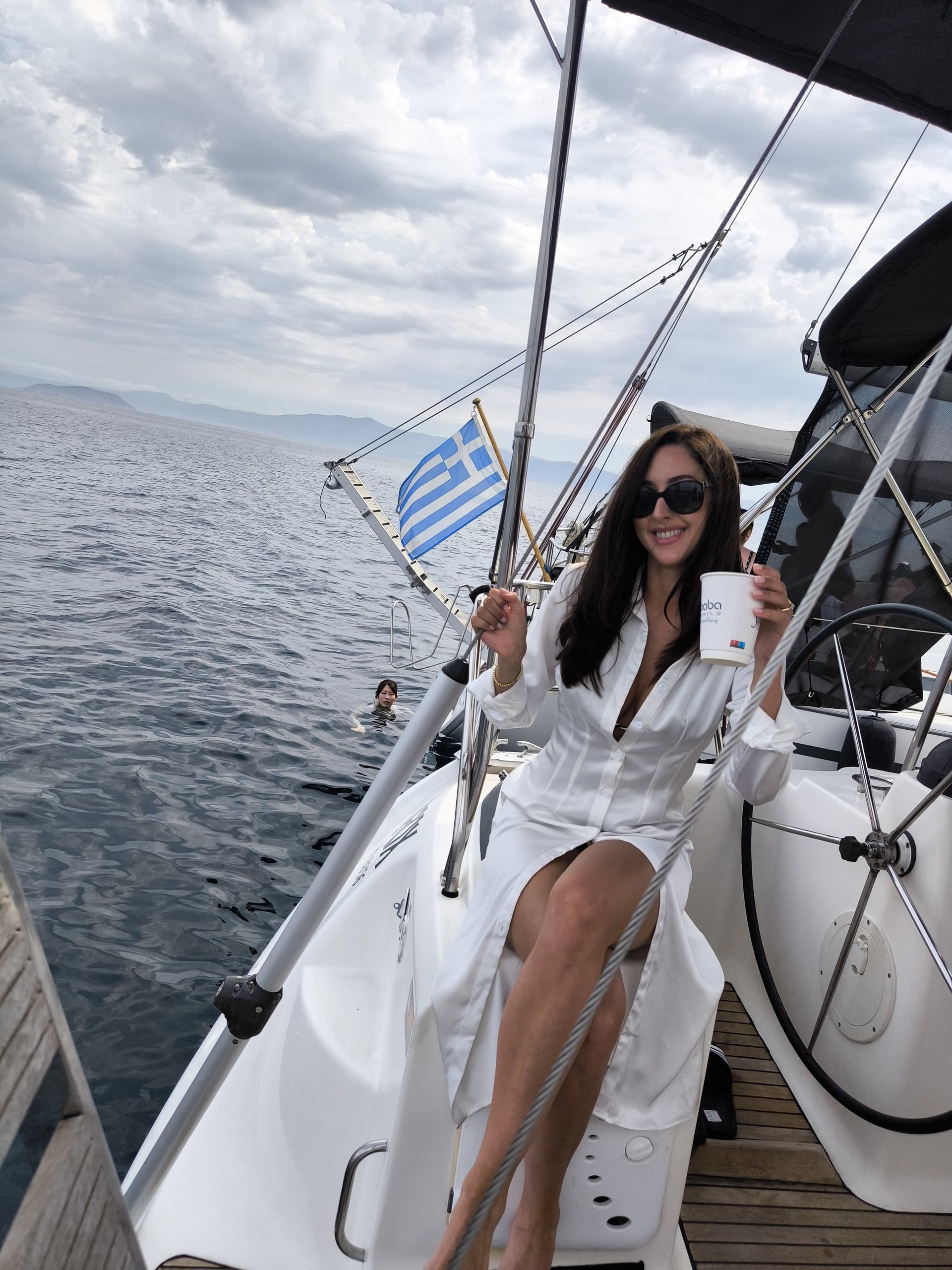 Woman in a white shirt sitting at a sailing yacht’s helm with a coffee